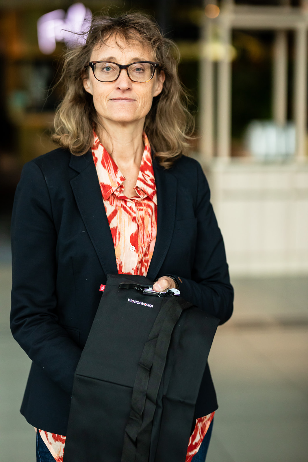 Anna Norlin, VD, WorqiWorqi. Klädd i jeans, röd skjorta, blå kavaj. Står loch håller ett svart förkläde och en vinöppnare i handen. Båda med Worqiworqi loggan på. Fotat i servicemiljö.